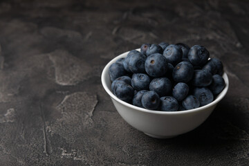 Blueberries in a ceramic bowl on a black textured background. Ripe and fresh blueberries. Vitamins. Healthy food. Juicy berry.Copy space.Place for text