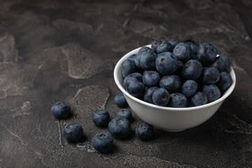 Blueberries in a ceramic bowl on a black textured background. Ripe and fresh blueberries. Vitamins. Healthy food. Juicy berry.Copy space.Place for text