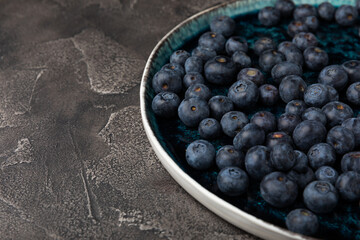 Blueberries in a ceramic bowl on a black textured background. Ripe and fresh blueberries. Vitamins. Healthy food. Juicy berry.Copy space.Place for text
