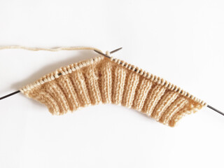 knitting on knitting needles from beige wool on a white background