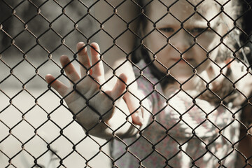 The child's hands are holding onto a metal mesh fence. The problem of forced deportation of...