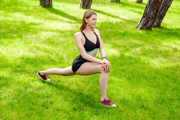Happy sportive woman wearing sports bra standing on city park, outdoors doing stretching workout. Stretching and motivation, outdoor sport concepts.