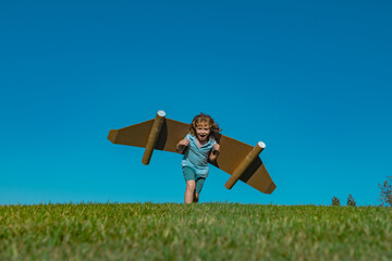 Kid with toy jetpack outdoor. Child playing in green spring field with cardboard wings. Spring travel and adventure. Kids success and leader, startup concept.