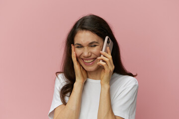  portrait of a woman in a white T-shirt holding a phone while talking and laughing emotionally while holding her hand near her face. Photo on an empty background with space for an advertising layout