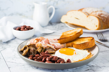 English breakfast with fried egg, bacon, beans, mushrooms and toast on a plate on the table.