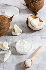 Fresh coconut oil in a jar and spoon and pieces of coconut on the table. Vertical view