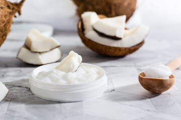 A piece of coconut in coconut oil in a jar and a wooden spoon with oil and coconut on the table.
