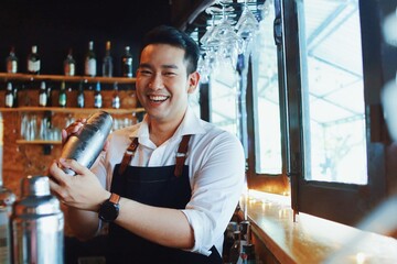 Handsome male bartender in apron preparing drink for customer at bar counter. Asian bartender man...