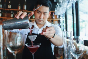 Handsome male bartender in apron preparing drink for customer at bar counter. Asian bartender man making some drink for guest of hotel.