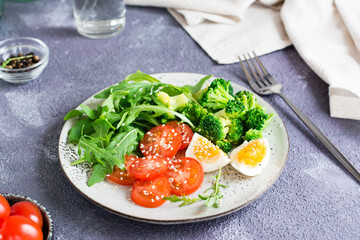 A plate with broccoli, arugula, tomato and boiled egg on a plate on the table. Ketogenic diet