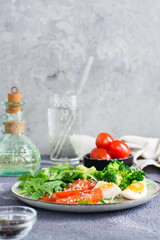 A plate with broccoli, tomato, arugula, boiled egg and sesame seeds on a plate. Vertical view
