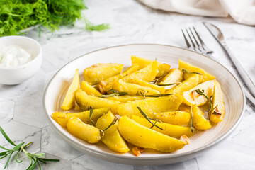 Baked potato wedges with garlic and rosemary on a plate on the table. Homemade vegetarian dish