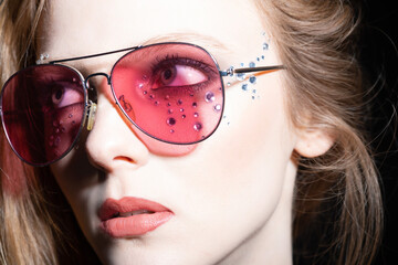 Beauty, fashion and make-up concept. Beautiful girl with pink retro sunglasses and long hair close-up studio portrait. Model with glued jewelers around her eyes looking aside the camera. Retro style