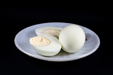 Hard boiled egg on white plate isolated on black background