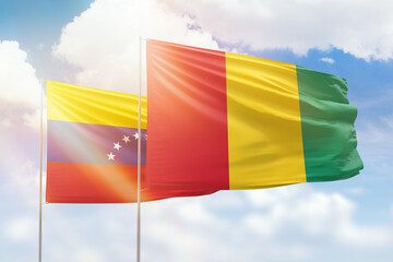 Sunny blue sky and flags of guinea and venezuela