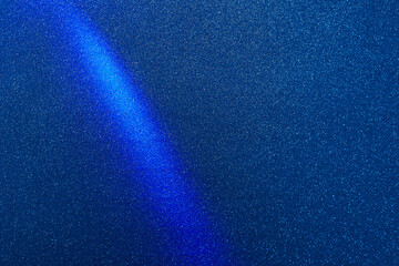 Blue diagonal beam of light on a dark blue background in fine white grain