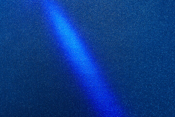 Bright blue diagonal beam of light on a dark blue background in fine white grain