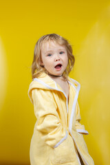 Baby girl blonde caucasian in a yellow terry bathrobe for bathing on a yellow background