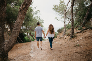 A photo from behind of a Hispanic man and his Latina girlfriend who are descending from the wooded...