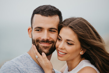 Fototapeta premium Close portrait of a Hispanic man and his smiling girlfriend who are cuddling up to each other on the rocky sea coast in a highland park in Spain. A happy couple of tourists in the evening in Valenci