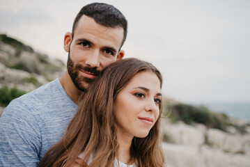 Obraz premium A close portrait of a Hispanic man who is hugging a Latina girl on the rocky sea coast in Spain. A couple of tourists in the evening in a highland park in Valencia.