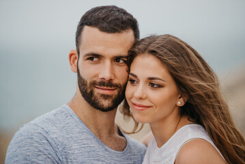 A close portrait of a Hispanic man and his Latina girlfriend who are cuddling up to each other on the rocky sea coast in a highland park in Spain. A couple of tourists in the evening in Valencia.