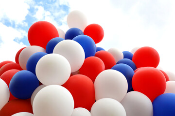 Helium balloons fly on background of sky with clouds. Red, blue and white festive background, colors of the French flag