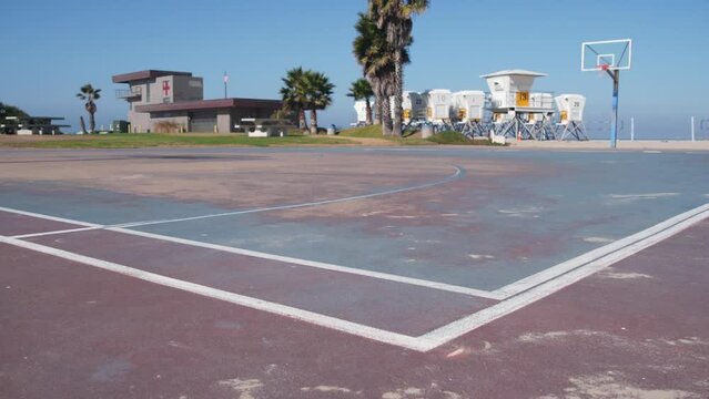 Palm trees and basketball sport field or court on beach, California coast, USA. Streetball playground on shore and lifeguard stand, tower ot station. Mission beach, San Diego. Hoop, backboard and sky.