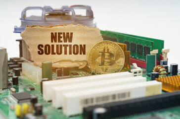 On the motherboard lies a bitcoin coin and a cardboard sign with the inscription - NEW SOLUTION