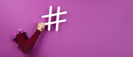 hand holding hashtag sign over pink background, social media concept, panoramic layout