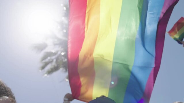 Slow motion of the rainbow flag waving with palm trees in the background during a pride parade