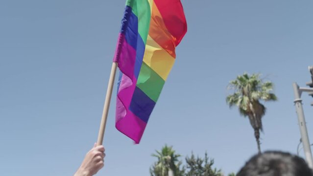 Slow motion of people waving the LGBTQ rainbow flag during a pride parade in a city streets