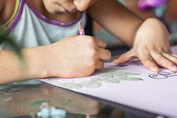 detailed view of a hand of a brown-skinned, low-income latina girl coloring with her colored...