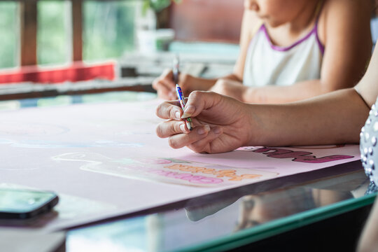 young latina mother teaching her daughter to paint with colored pencils, woman doing school homework with her young daughter. detailed view of a girl's hand holding a pencil to paint on the poster.