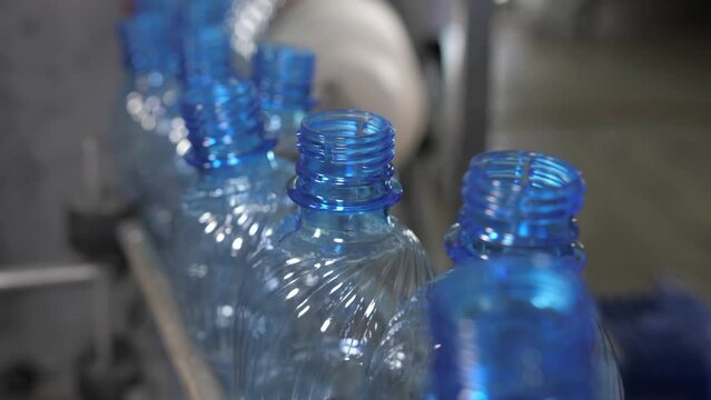 Close up of empty blue plastic bottles moving on a conveyor belt. Mineral water production plant.