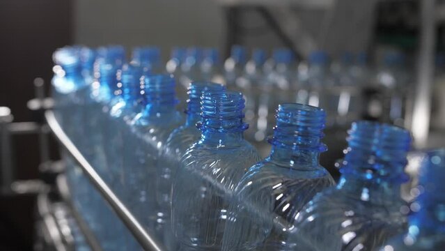 Empty blue plastic bottles are moved on a conveyor belt. Mineral water production plant.