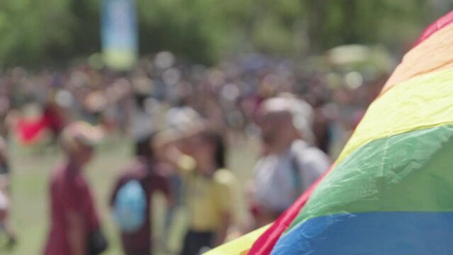 The LGBTQ rainbow flag waving in slow motion with people in a pride parade in the background
