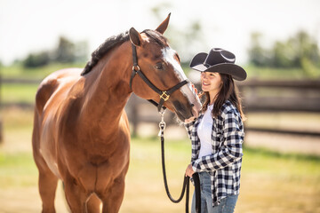 A bond between a horse and a young woman in cowboy hat on a ranch outdoors