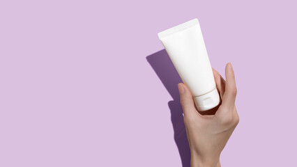Young female hands holding blank white squeeze bottle plastic tube on pink background. Packaging of cream, lotion, gel, facial foam or skincare. Cosmetic beauty product branding mock-up. Copy space