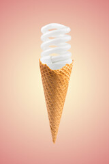 Compact fluorescent bulb in ice cream cone. Pink background. Creative summer concept