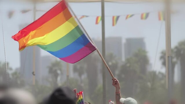 LGBTQ rainbow flag waving in slow motion during the main party in a pride parade with thousands of people