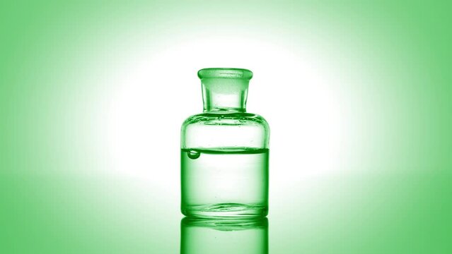 Green drop is falling into old fashioned bottle with green clear liquid on green background | Abstract skin care cosmetics with aloe vera extract formulating concept