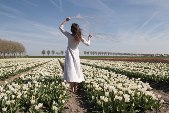 Happy woman in white dress dancing in a field of tulip flowers in spring