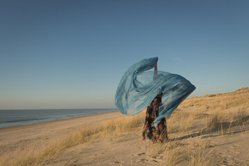 woman in floral dress dancing on the beach hlding fabric in the wind