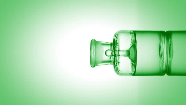Drop of citric acid falls into old fashioned bottle with green transparent fluid on green background | Abstract body care cosmetics with citric acid mixing concept