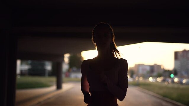 A young woman runner is training in the summer within a city. Close up of silhouette fitness girl is jogging outdoor. Concept of workouts running and healthy lifestyle. Slow motion.