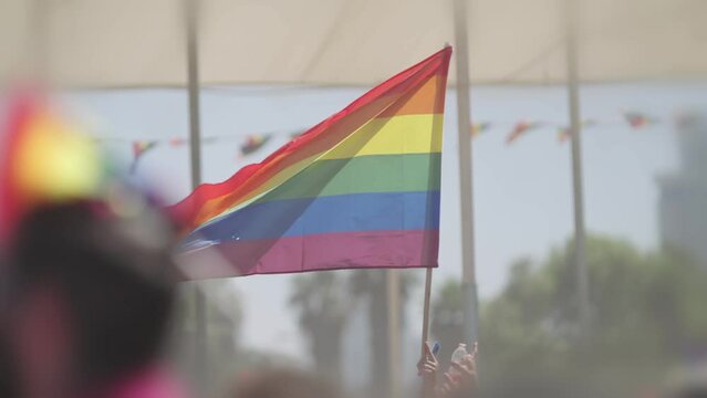 LGBTQ rainbow flag waving in slow motion during the main party in a pride parade with thousands of people