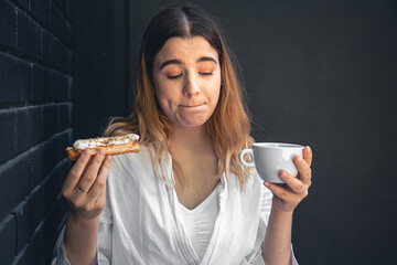 A young woman with a cup of coffee and an eclair in her hands.