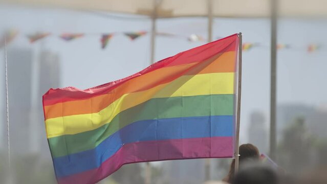 LGBTQ rainbow flag waving in slow motion during the main party in a pride parade with thousands of people
