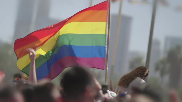 LGBTQ rainbow flag waving in slow motion during the main party in a pride parade with thousands of people